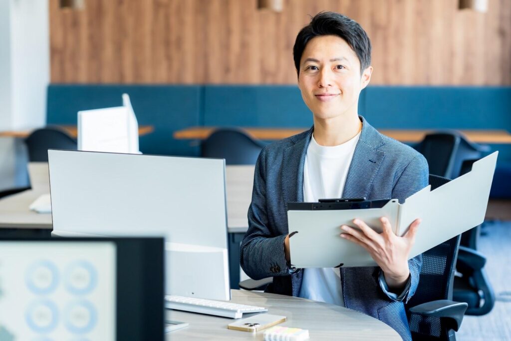 パソコンとファインダーを持ってこちらを見る男性