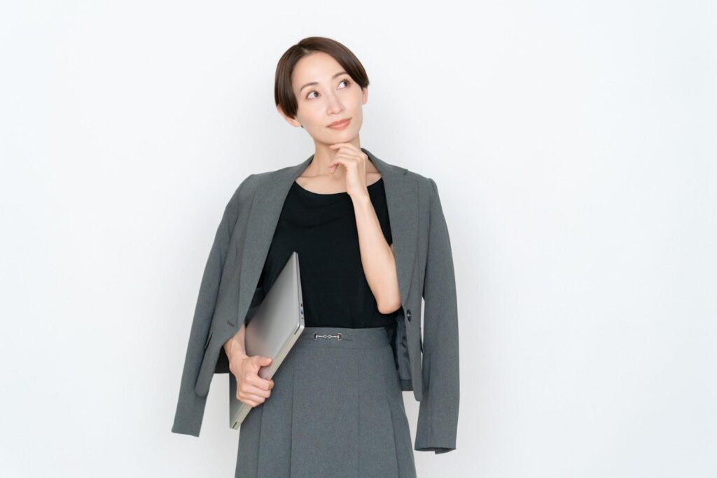 パソコンを片手に考えるオフィスカジュアルの中年女性