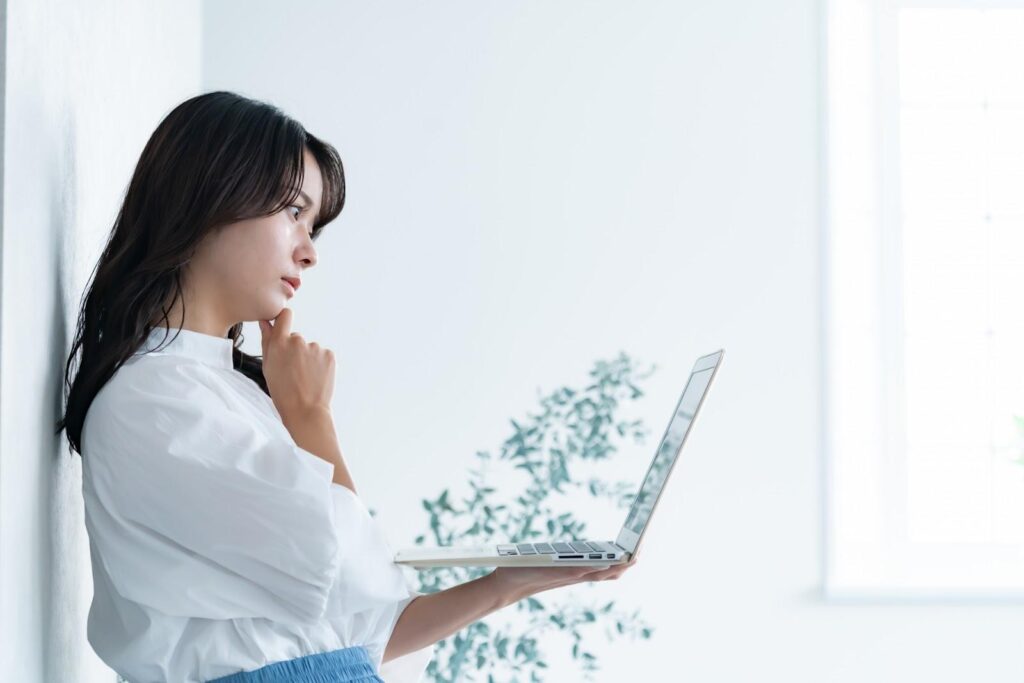 パソコンを見ながら考える白服の女性