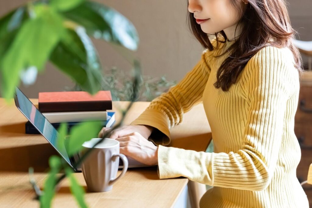 ノートパソコンと書籍を置いて作業する私服女性