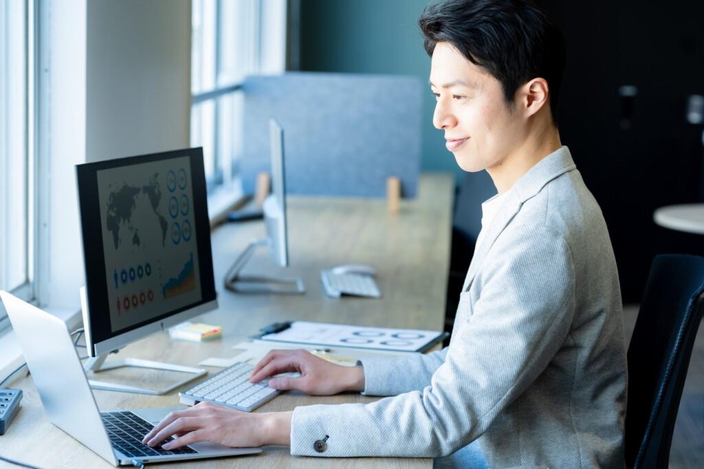 2つのパソコンを見ながら作業する男性