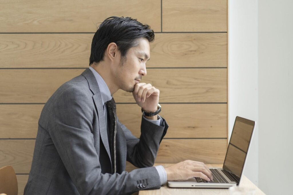 パソコンを見て考える灰色スーツの中年男性