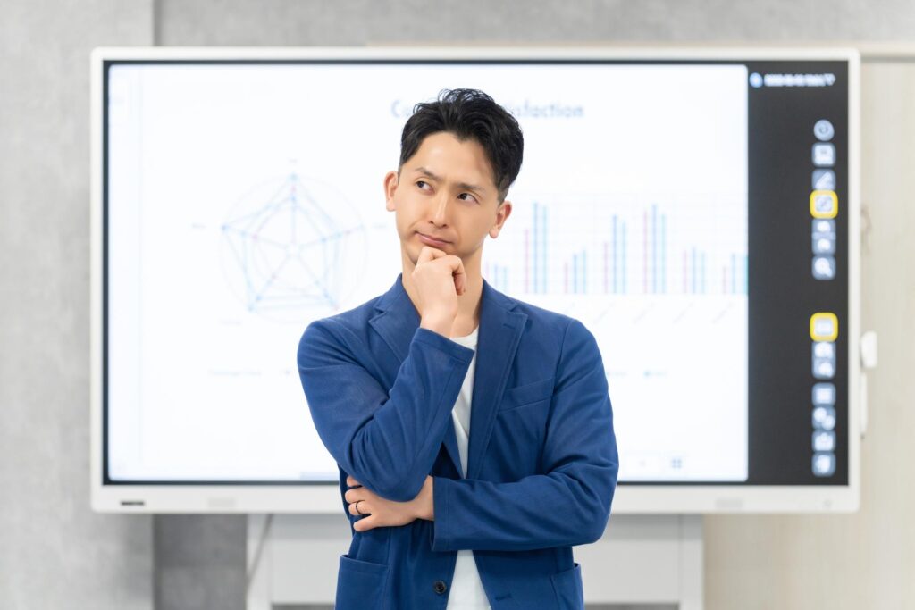 スクリーン背景にして腕を組んで考え事をする青スーツの男性