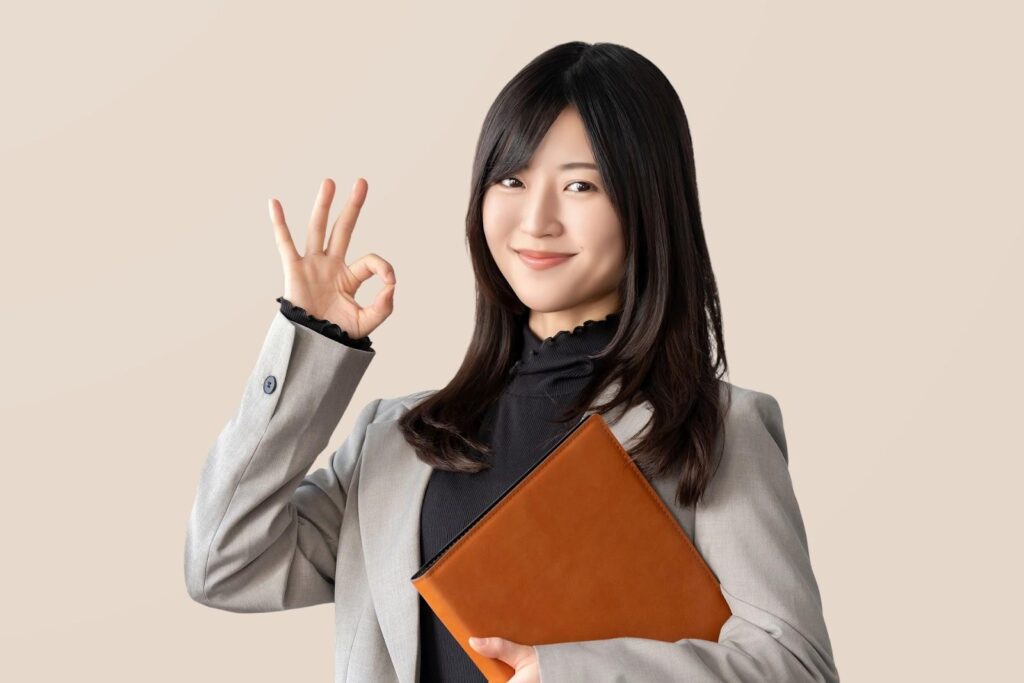 明るいブラウン色のファインダーを持ちながらOKマークを作るオフィスカジュアル姿の女性