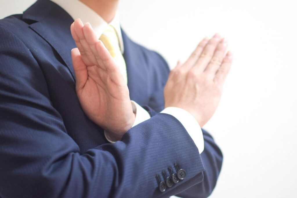 両腕でバツ印を作りながら注意を促すスーツ姿の男性