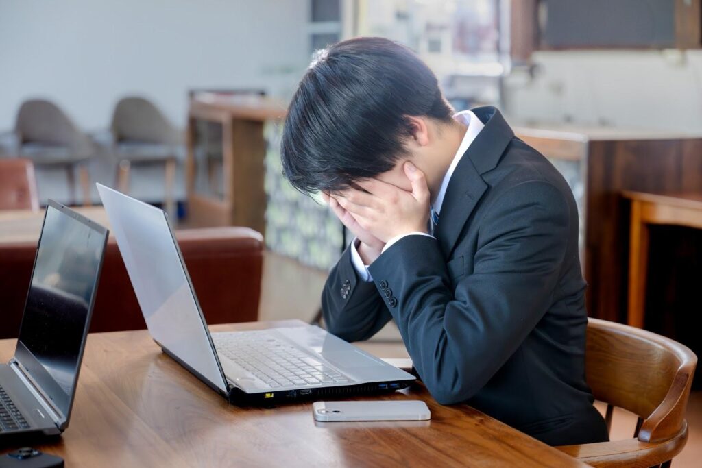 両手に顔をうずめてパソコンの前で悩んでいるスーツ姿の男性