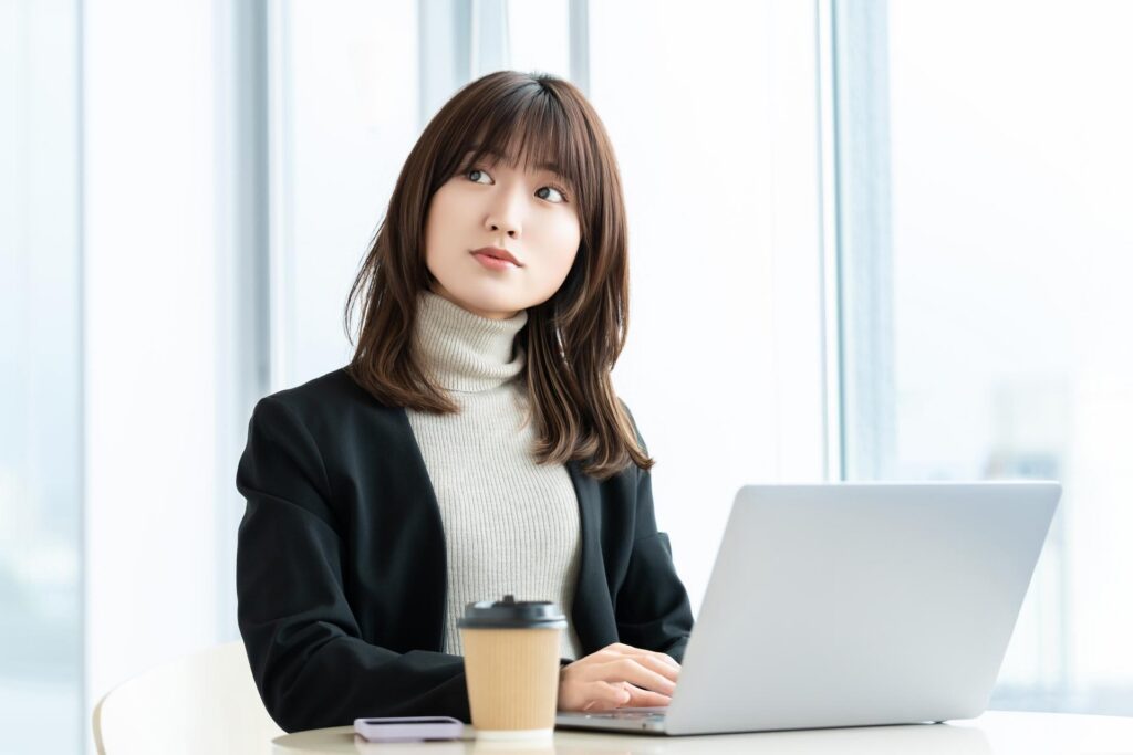 カフェでコーヒーを飲みながらパソコン作業する若い女性