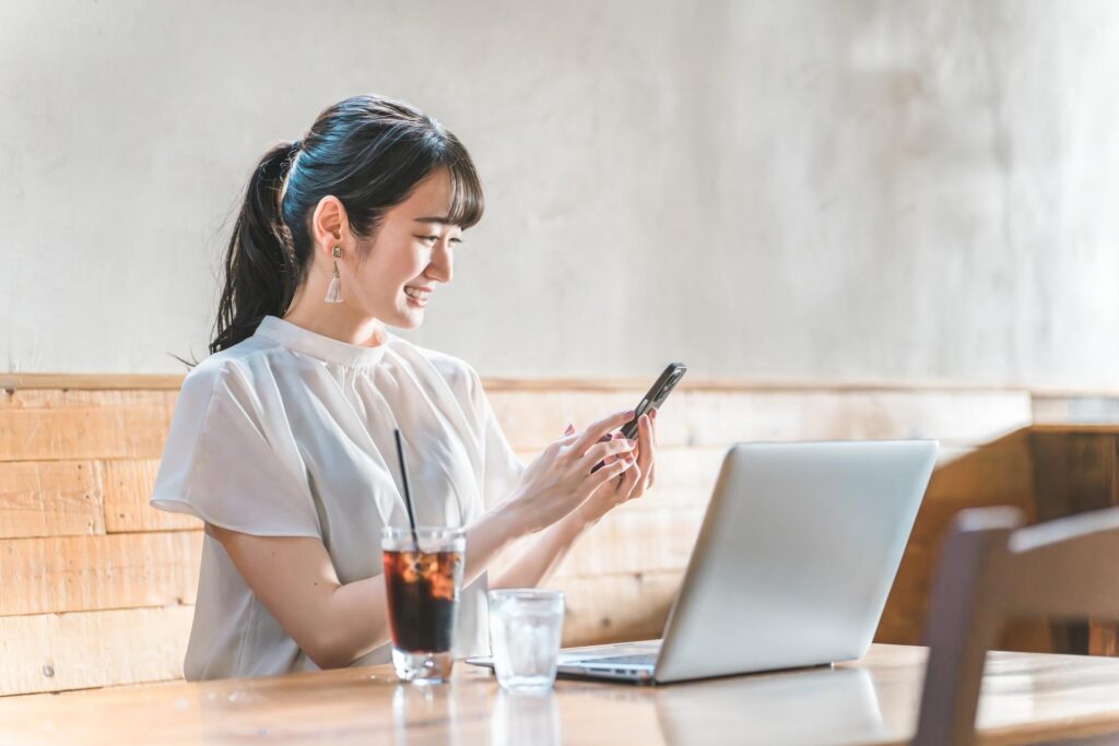 カフェでパソコンとスマホを見ながら嬉しそうな表情を浮かべる若い女性