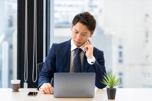 パソコンを開いて何を考えているスーツ姿の男性