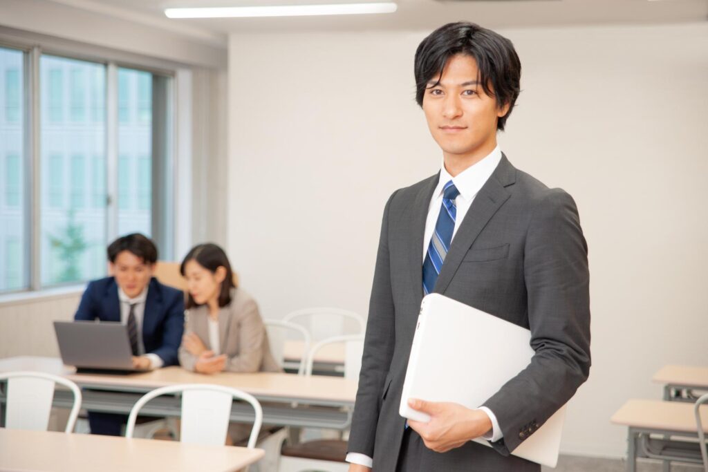 パソコンを片手にこちらを見るスーツ姿の男性
