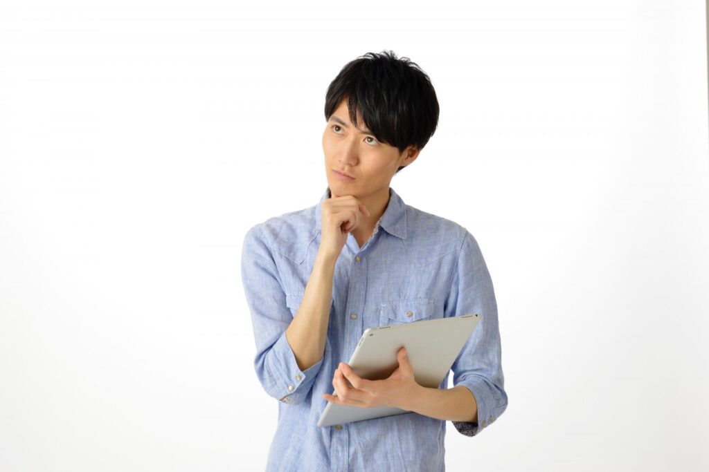 パソコンを片手に持ちながらFXのデメリットについて考える細身の男性