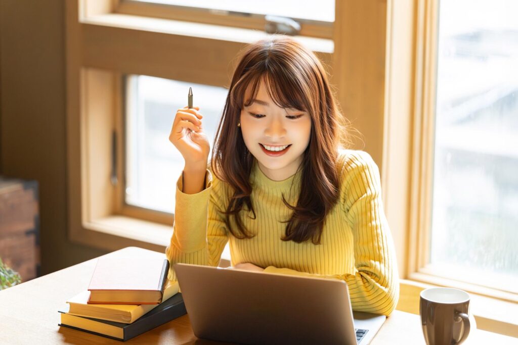 図書館でパソコンと本を開きながら嬉しそうな表情を浮かべる私服の女性