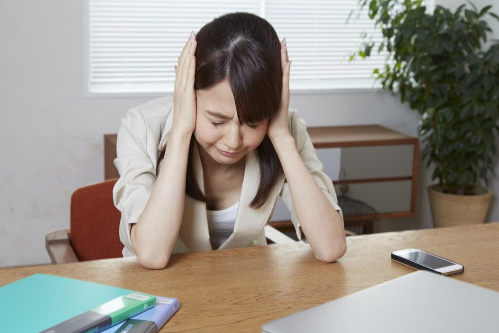 目をつむり耳を両手で塞いで悩んでいる女性