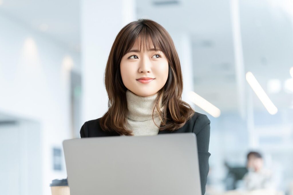 パソコンを開きながら横目で遠くを見る丸顔の若い女性