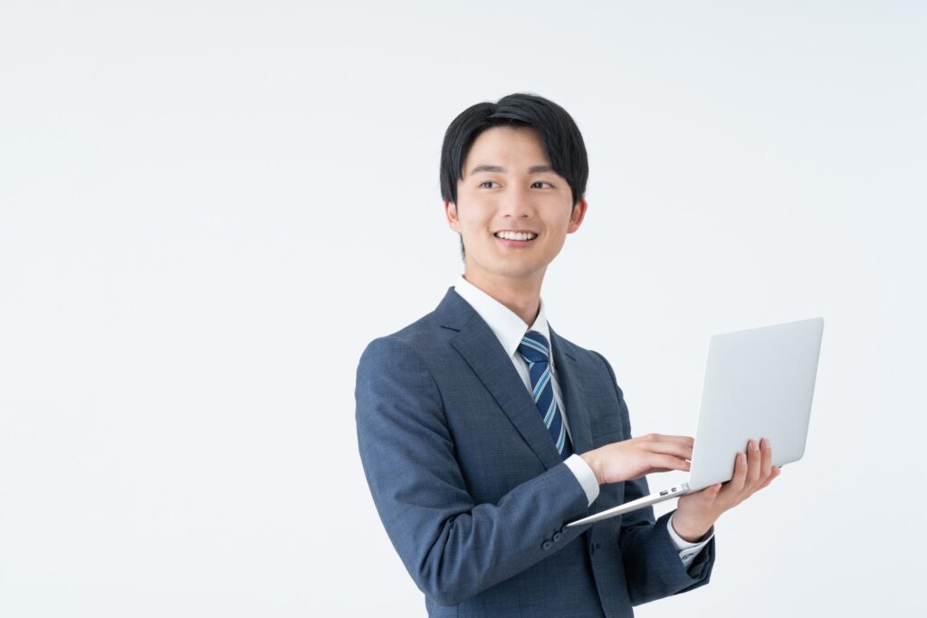 パソコンを片手に持ちながら微笑むスーツ姿の若い男性