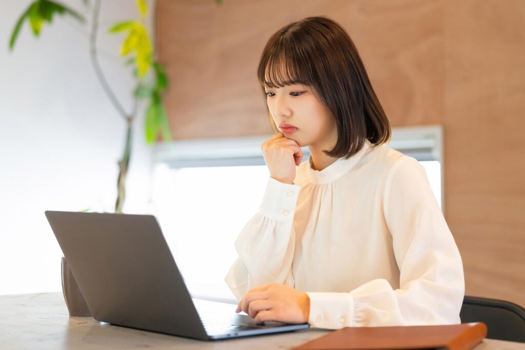 自宅でパソコンを見つめながら疑問を抱いている女性