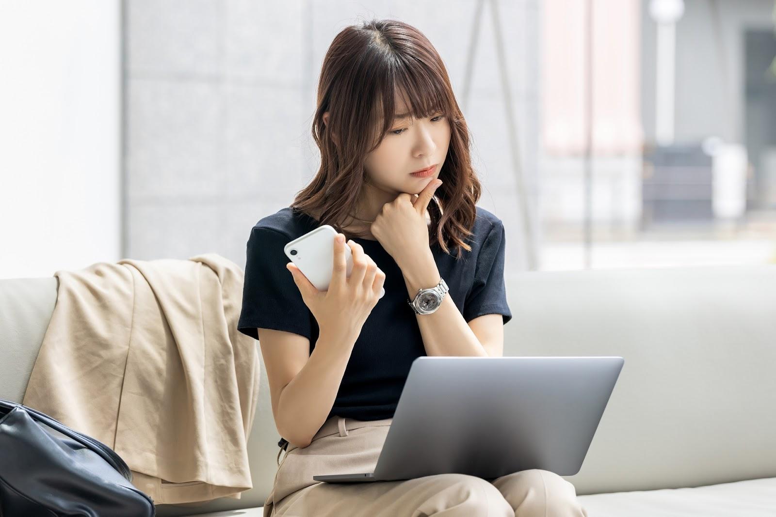 スマホとパソコンを見比べながらFX取引を検討する女性