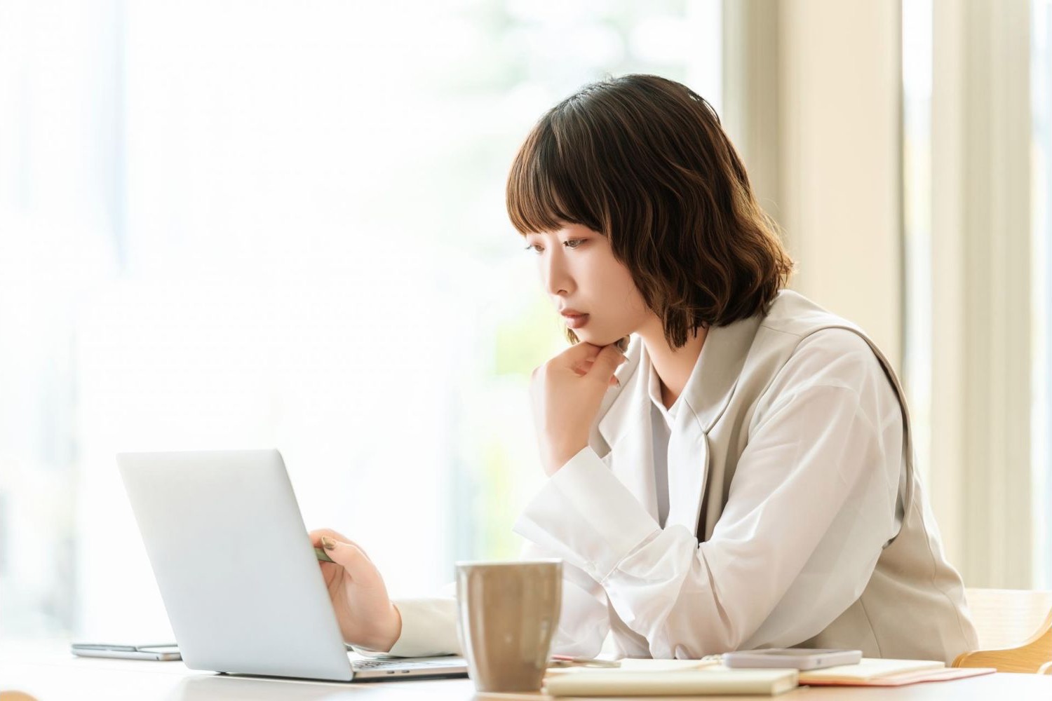 自宅の机でノートパソコンを見ながら考える女性