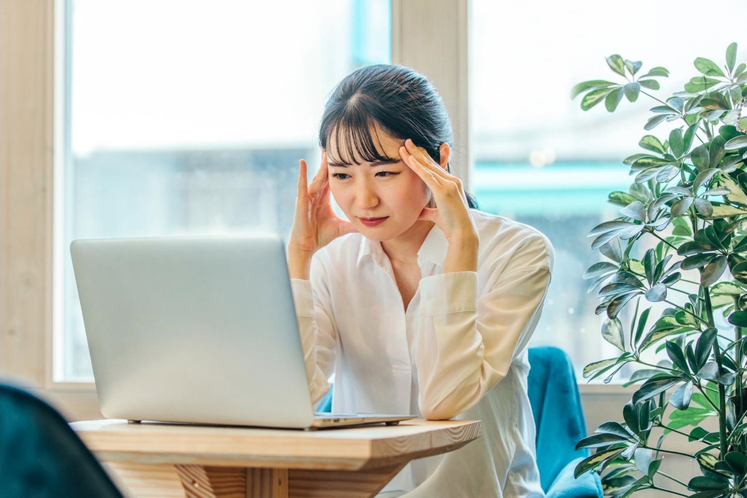 ノートパソコンの前でこめかみを押さえる女性