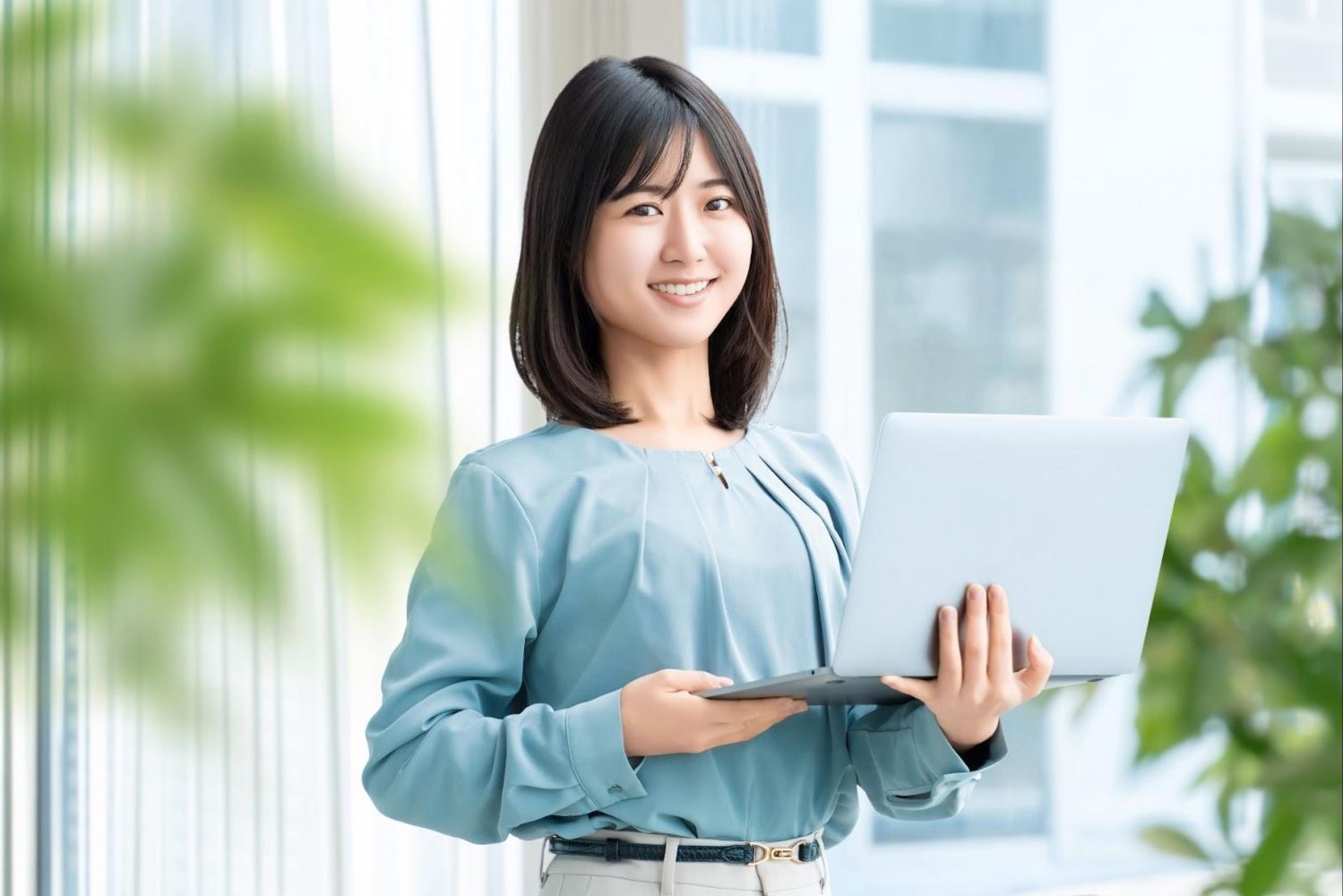 ノートパソコンを手に笑顔で立つ女性会社員