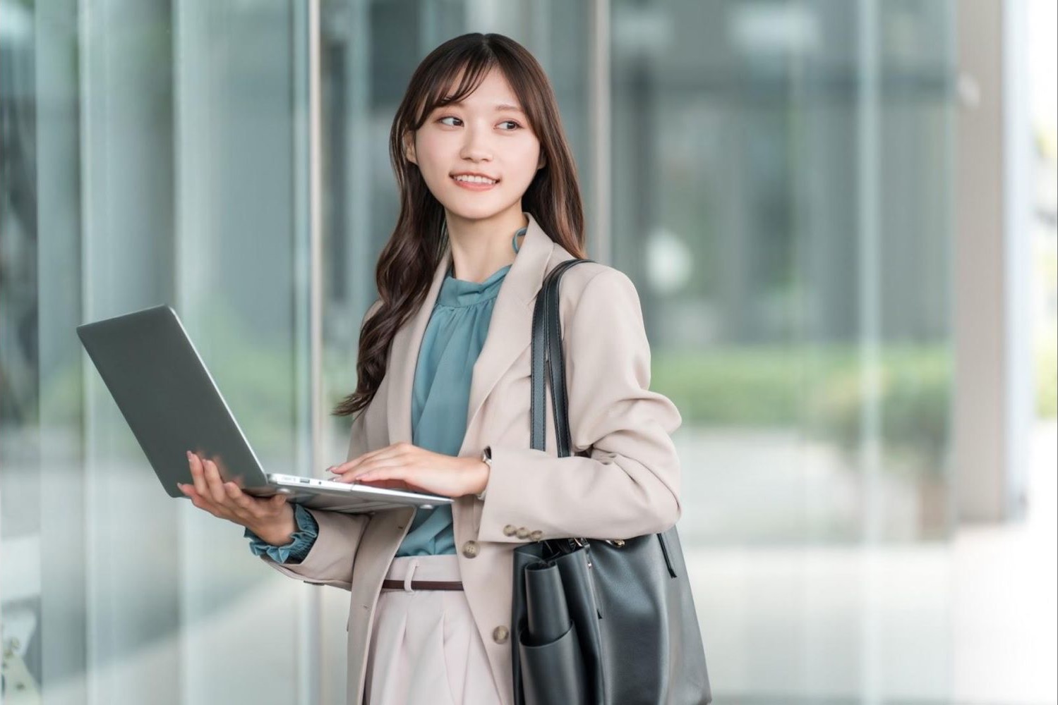 ノートパソコンを持ち、手のひらで案内する女性会社員