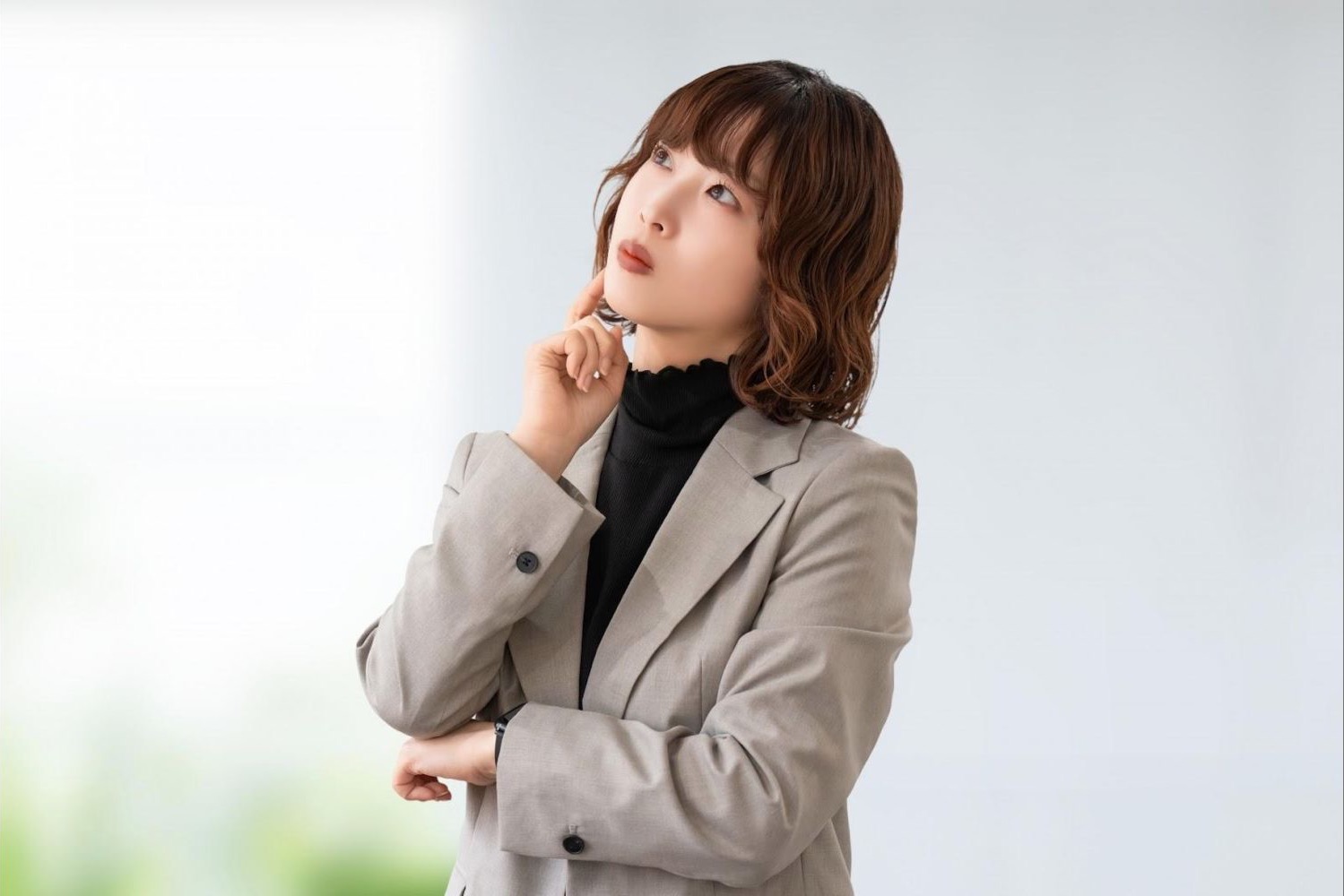 腕を組み、首をかしげて考える女性会社員