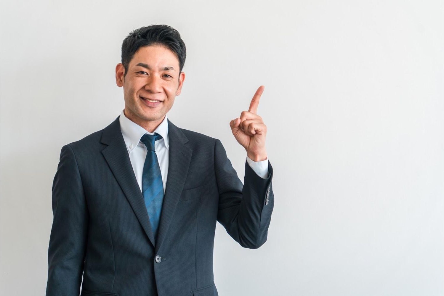 正面を向き、人差し指を立てる男性会社員