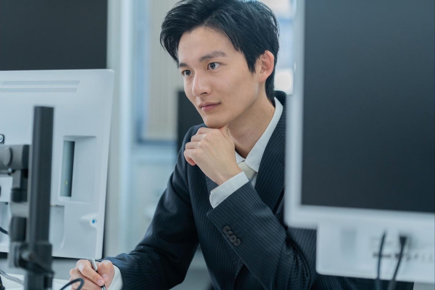 複数のモニターを見ながら考える男性会社員
