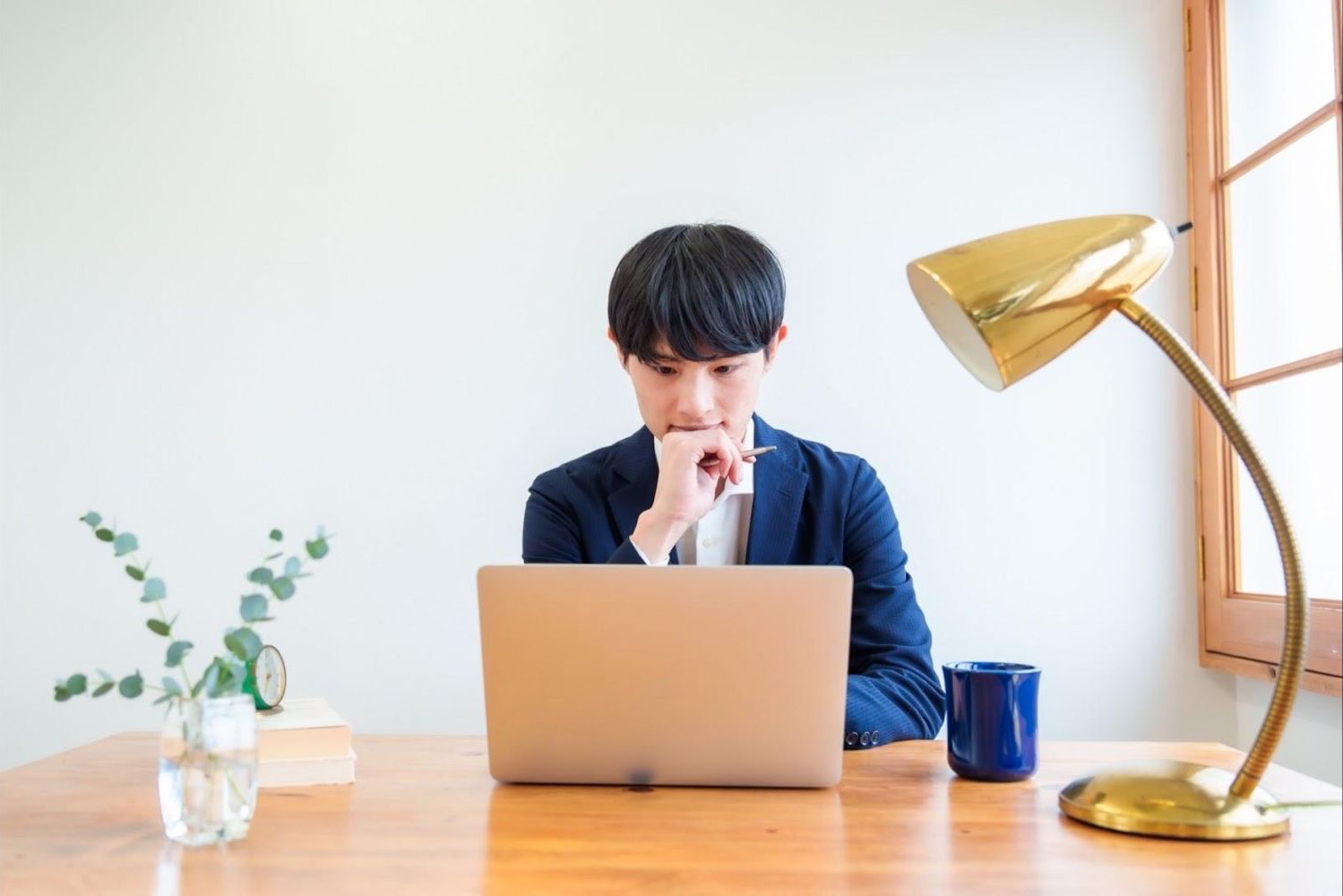 照明のある机でノートパソコンを見ながら考える男性