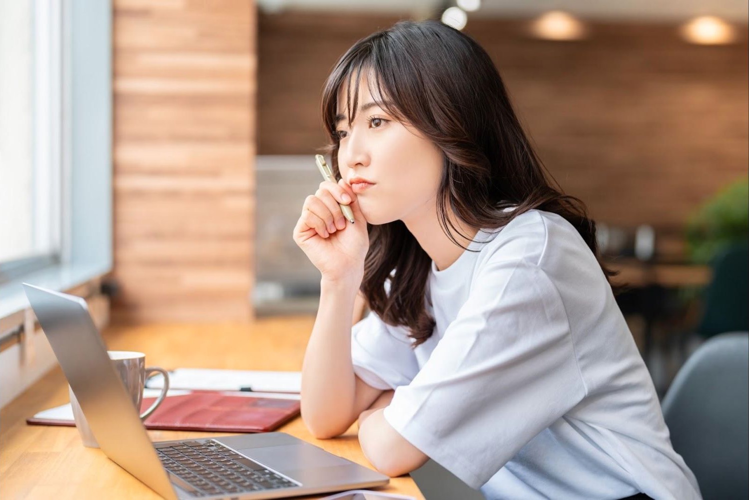カフェでノートパソコンを見ながら考える女性