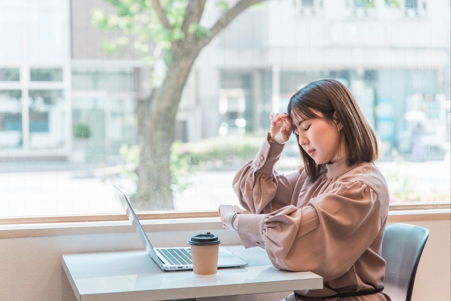 窓際の席で資料を見ながら頭を押さえる女性