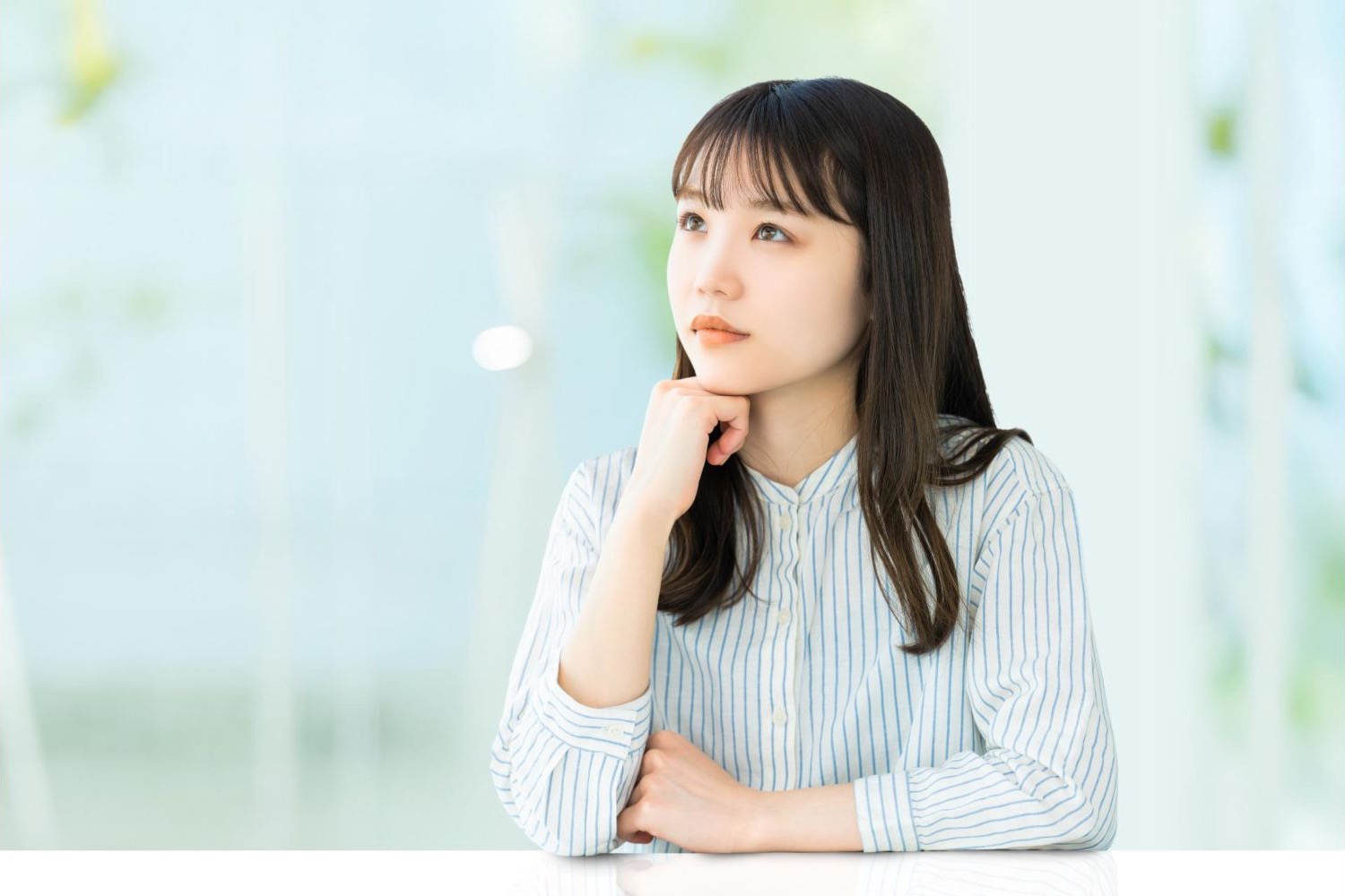 顎に手を当て、上を見ながら考える女性