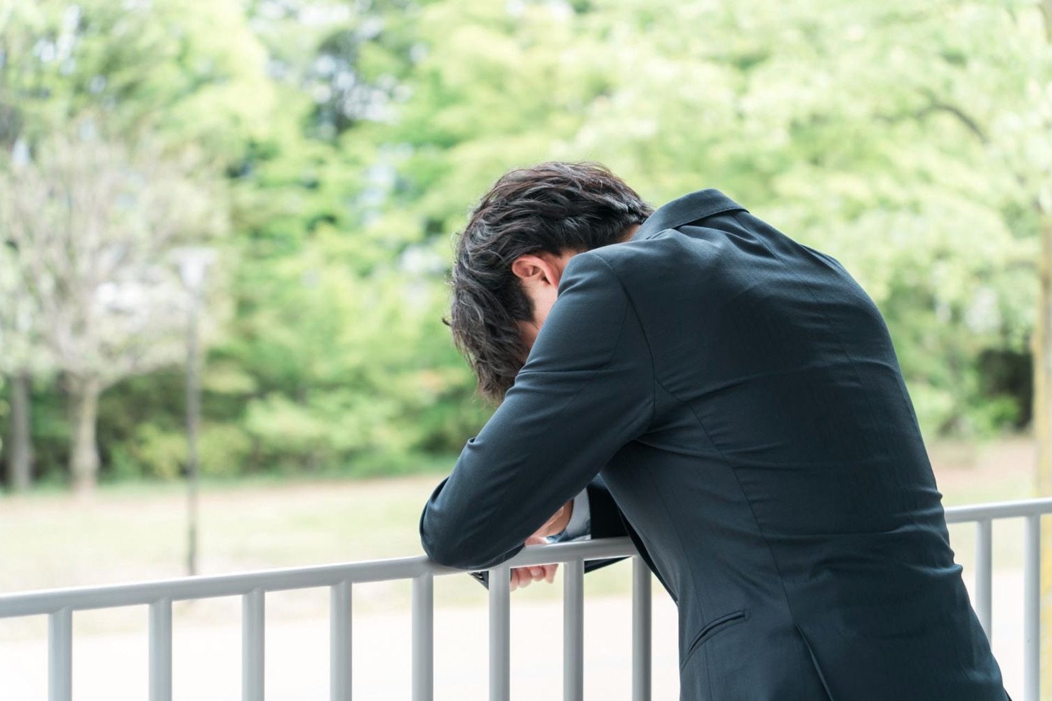屋外の手すりにもたれて頭を伏せる男性