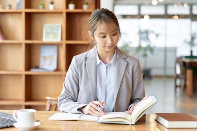カフェの机で本を開き、ノートに書く女性