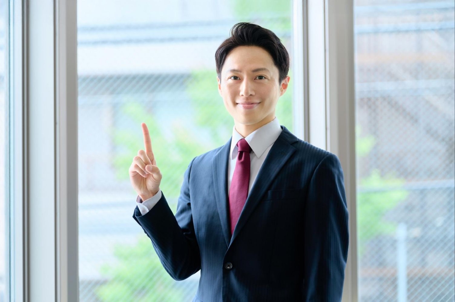 窓辺で人差し指を立てる男性会社員