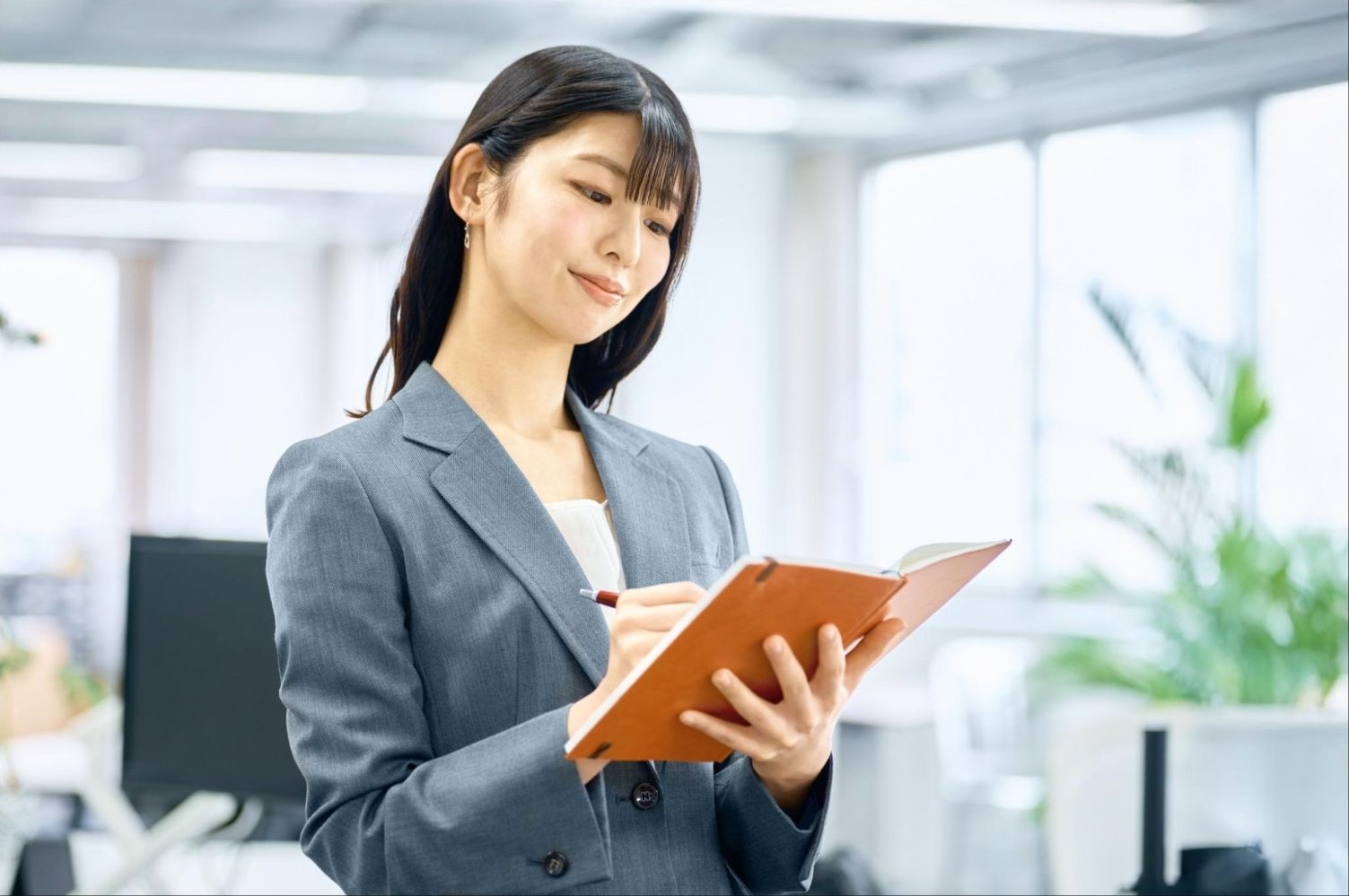 オレンジ色の手帳を持って確認する女性会社員