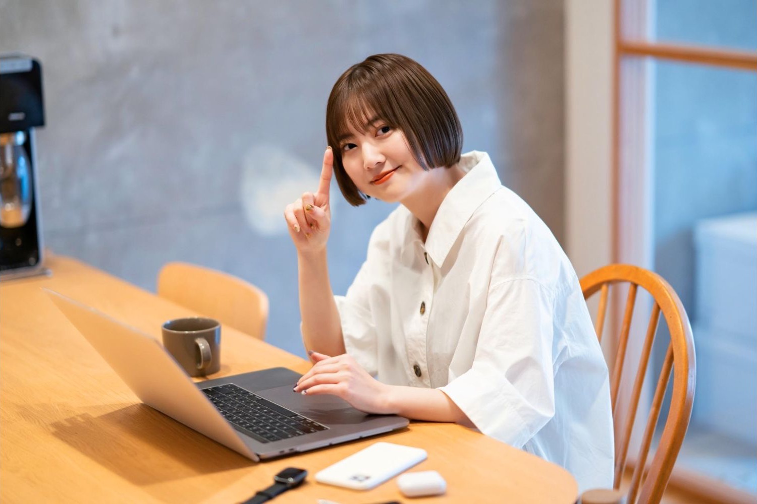 木製の机でノートパソコンを使い、人差し指を立てる女性