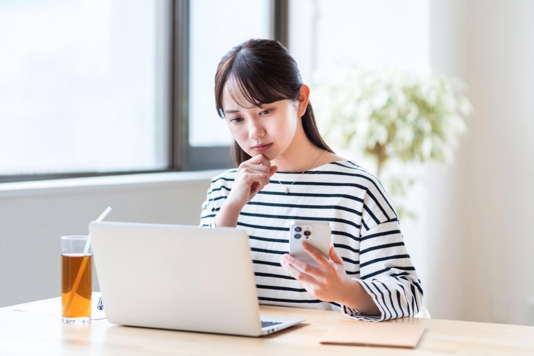 自宅の机でノートパソコンを見ながら考える女性