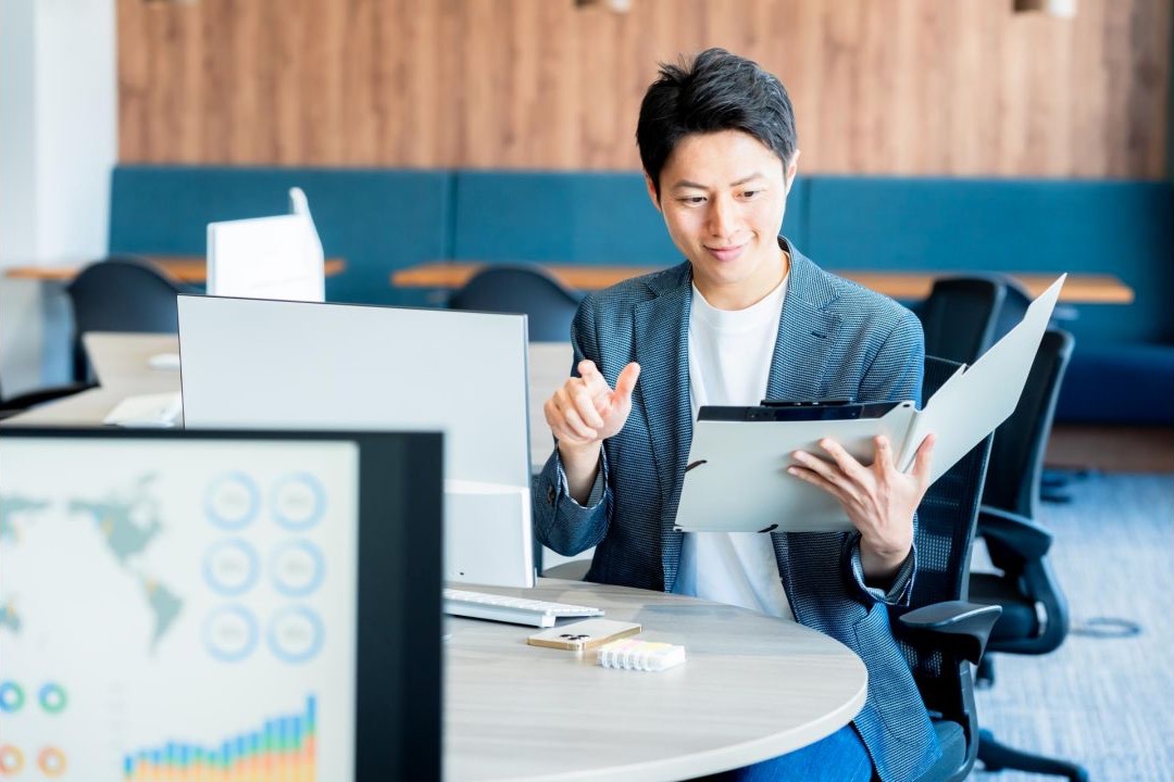 複数の資料とタブレットを見ながら説明する男性会社員