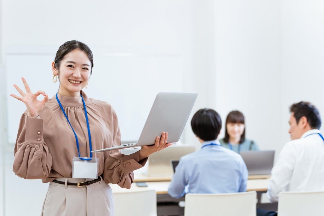 ノートパソコンを持ち、手で丸印を作る女性会社員