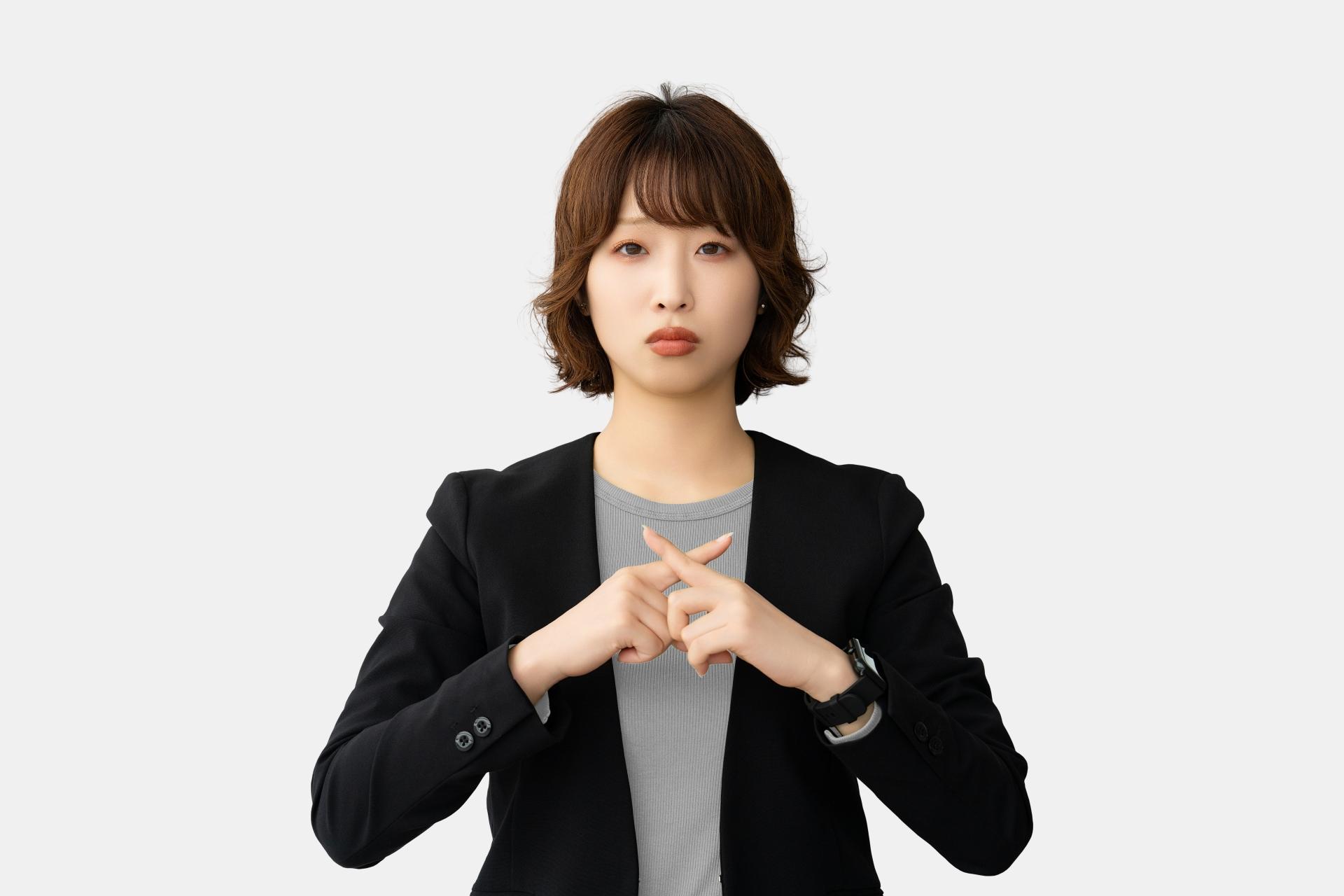 指でバツのポーズをする困った表情の女性