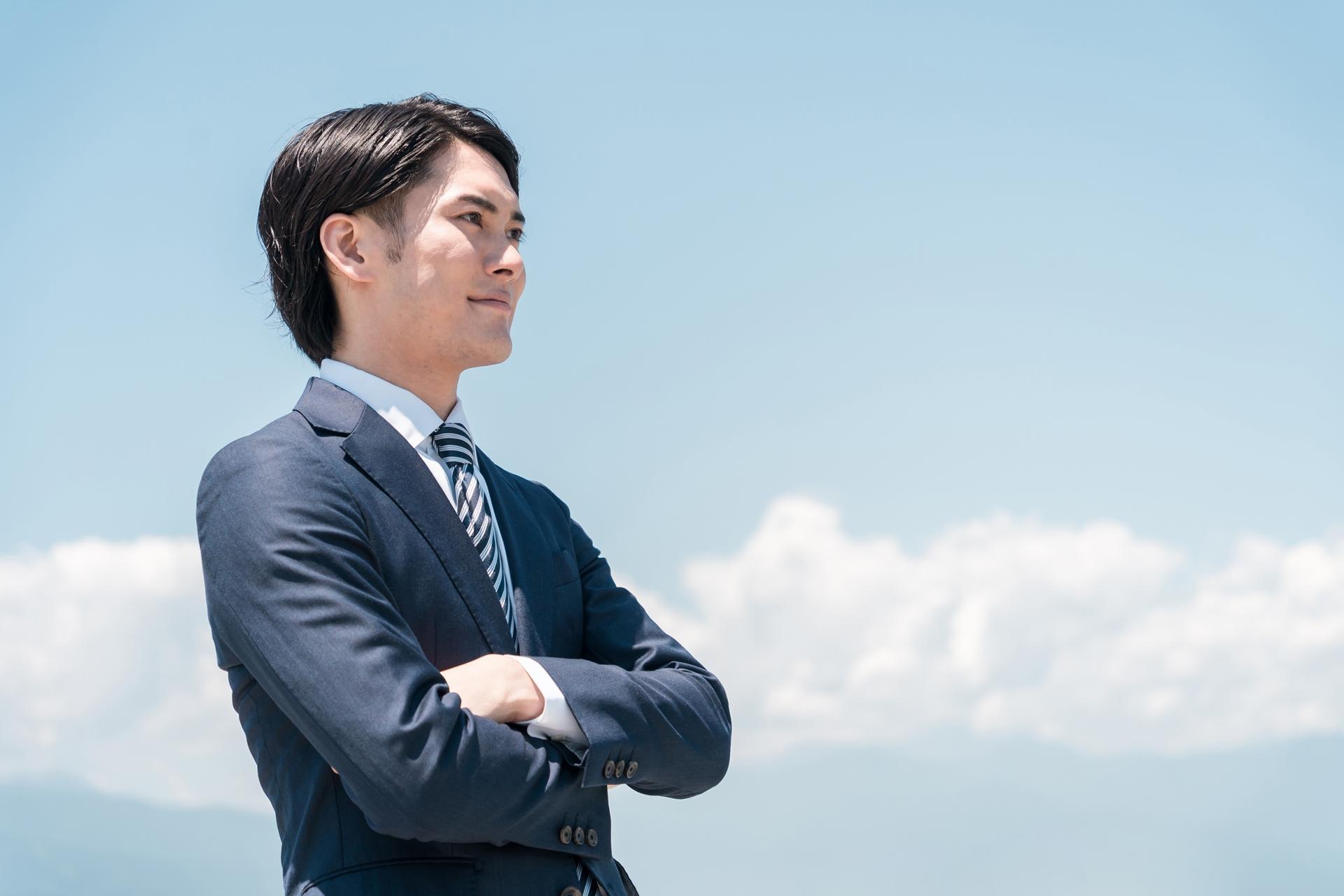 青空の中で腕組みする笑顔のビジネスマン